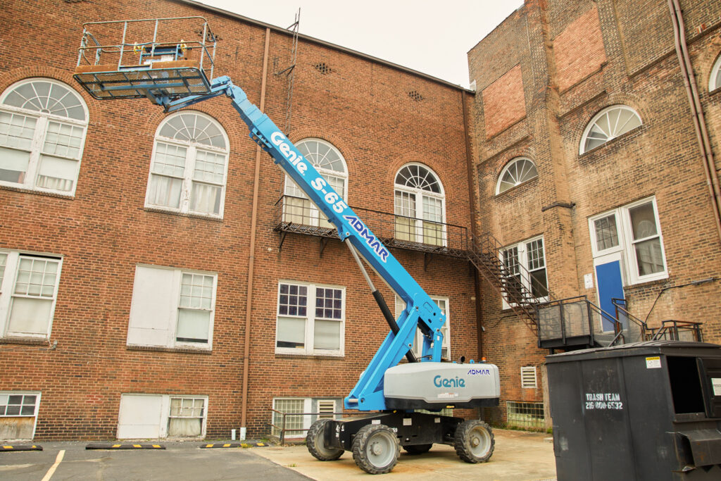 A bright blue electric bucket lift sits in front of the exterior of Cory United Methodist Church