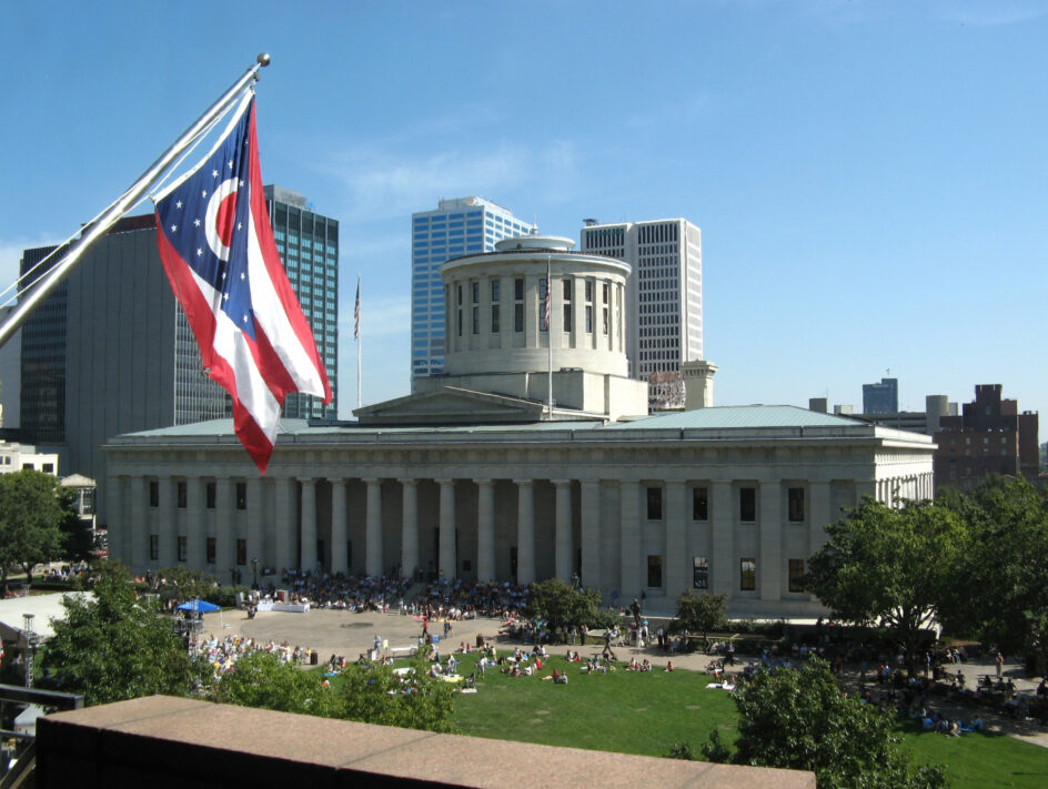A view of the Statehouse with the Ohio state flag flying in the foreground, seen from the Riffe Center on Symphony Week 2007. The crowd is listening to the Columbus Symphony Orchestra.